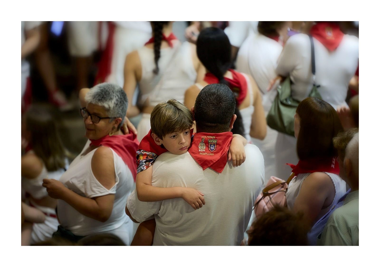 Un hombre con un niño en brazos entre la multitud vestida de blanco y rojo en San Fermín
