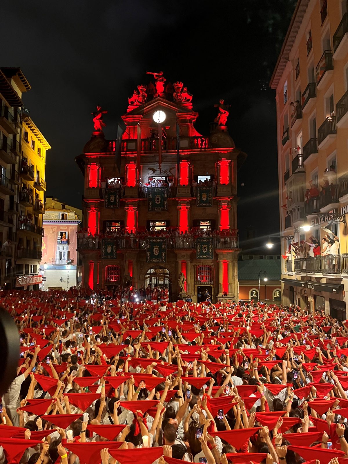 Pañuelos rojos al aire frente al Ayuntamiento de Pamplona iluminado durante el Pobre de mí