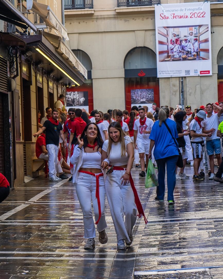Paseo por Pamplona durante las fiestas de San Fermín Dos amigas vestidas de blanco y rojo ríen por una calle de Pamplona durante San Fermín