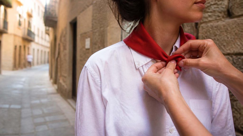Persona anudando un pañuelo rojo sobre ropa blanca durante las fiestas de San Fermín en Pamplona
